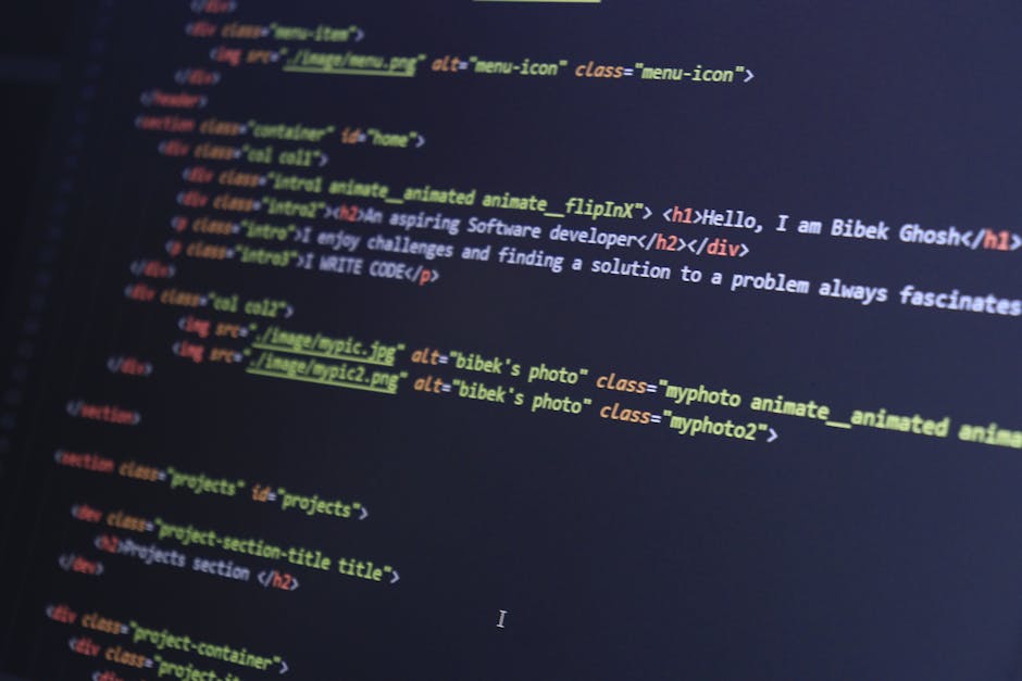 A person's hand, wearing a wristwatch, is seen typing on a laptop keyboard placed on a wooden desk. The laptop screen displays lines of code with colorful syntax highlighting. The desk has a smooth, n